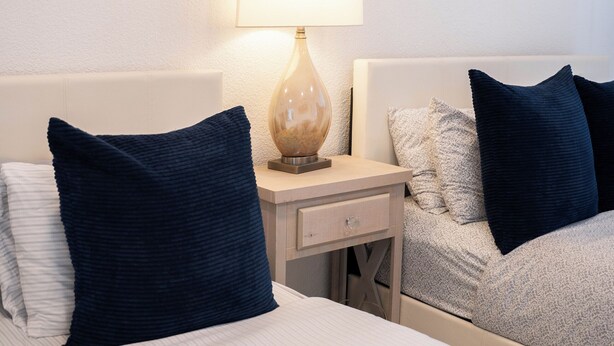 A hotel room with two beds, a nightstand with a lamp, and wall art. - Da Vinci Suites 702 (San Juan)