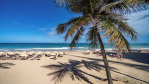 A beach with palm trees, sun loungers, and umbrellas. - Da Vinci Suites 702 (San Juan)