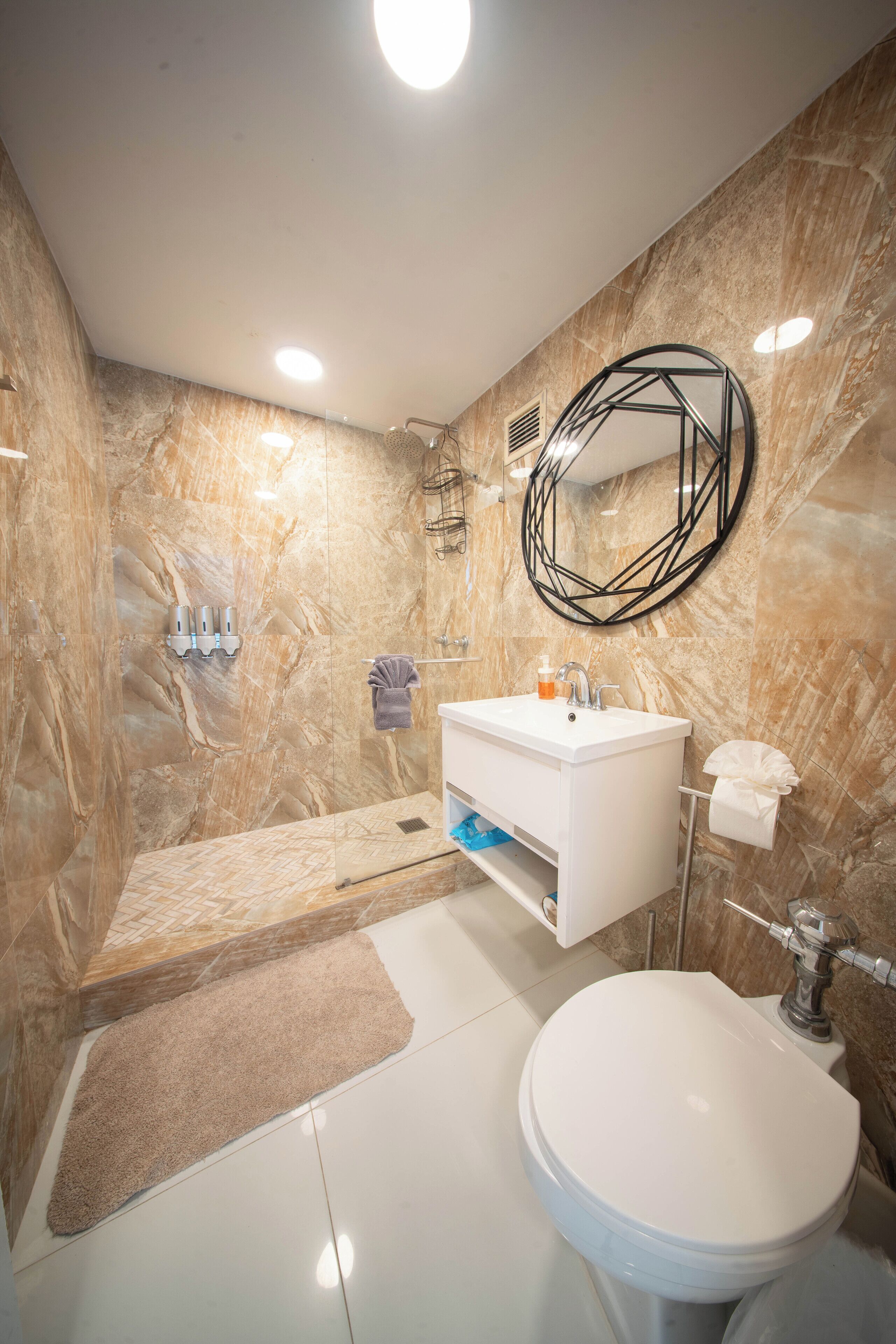 Ein modernes Badezimmer mit Marmorwand, Waschbecken in Weiß, Toilette und Duschbereich.
