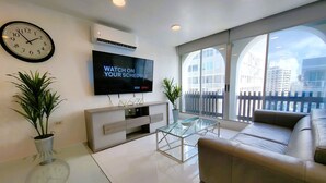A modern living room with a flat-screen TV, a sofa, a coffee table, and a large window with a view of buildings.