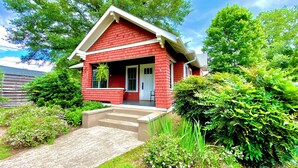A red house with a front porch, surrounded by greenery and trees. - Deluxe Downtown Bungalow - fenced in yard, pet friendly. (Brevard)