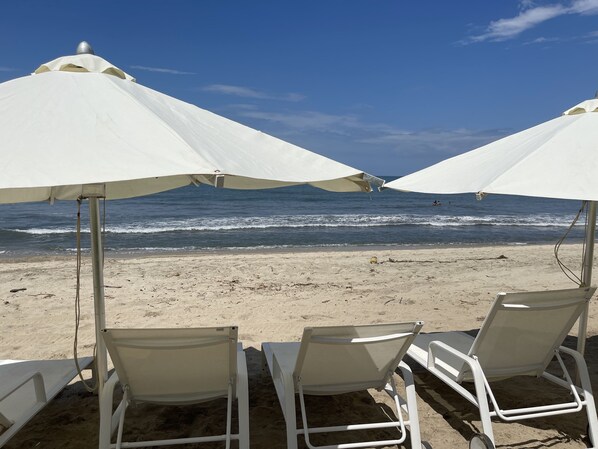 Beach umbrellas and lounge chairs on a sandy beach with the ocean in the background.