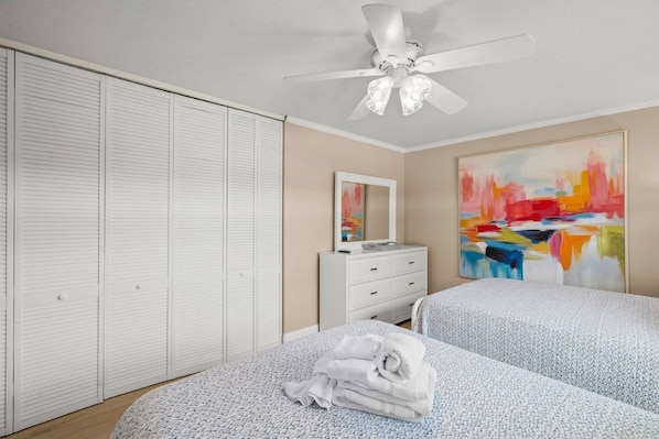 A bedroom with two beds, a white dresser, a ceiling fan, and a large abstract painting on the wall.