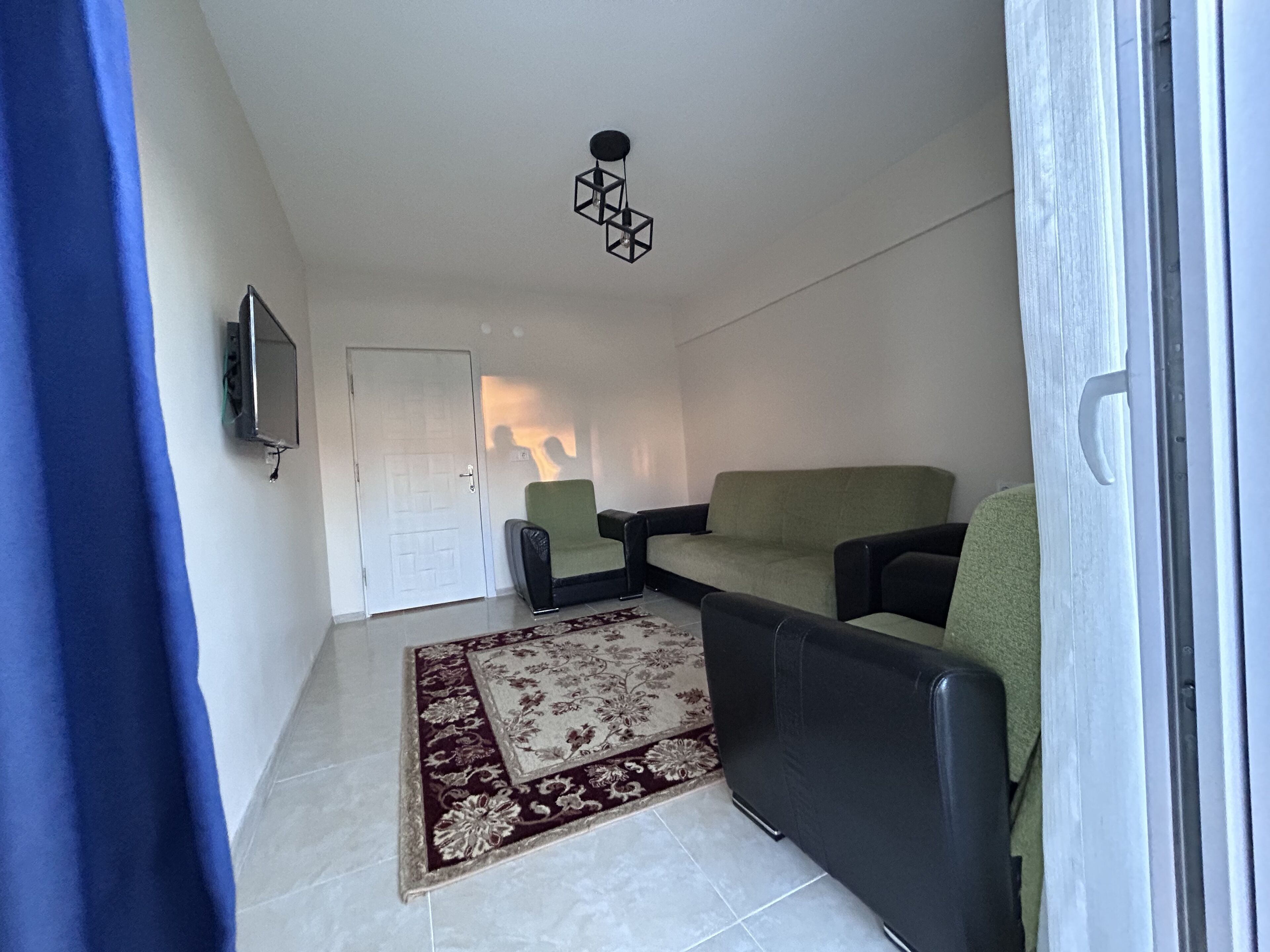 Un salon comprenant un canapé, deux fauteuils, un téléviseur et un tapis à motifs.