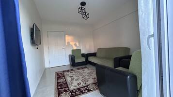 Un salon comprenant un canapé, deux fauteuils, un téléviseur et un tapis à motifs.