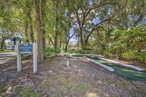 A miniature golf course sign with a start point arrow, surrounded by trees and greenery.