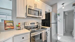 A modern kitchen with white cabinets, stainless steel appliances, and a large window. - Enchanted Cottage with Pool and Mini-Golf Near Disney (Kissimmee)