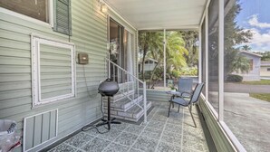 A covered porch with a grill, chairs, and a view of the neighborhood. - Enchanted Cottage with Pool and Mini-Golf Near Disney (Kissimmee)