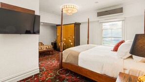 Una habitación de hotel con una cama grande, un televisor montado en la pared, un candelabro y una ventana con vistas.