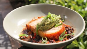 A bowl of food with a slice of meat, beans, and a green topping.