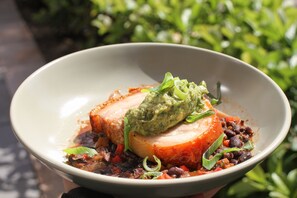 A bowl of food with a slice of meat, beans, and a green topping.