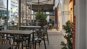 Un área de café al aire libre con mesas y sillas, una maceta grande y vistas a la calle.