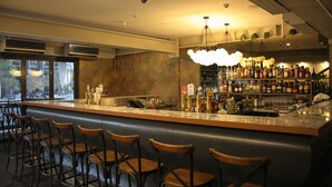 Una zona de bar con mostrador, taburetes y una variedad de botellas y vasos.