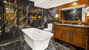 A modern bathroom with a freestanding bathtub, a vanity with a large mirror, and marble walls.