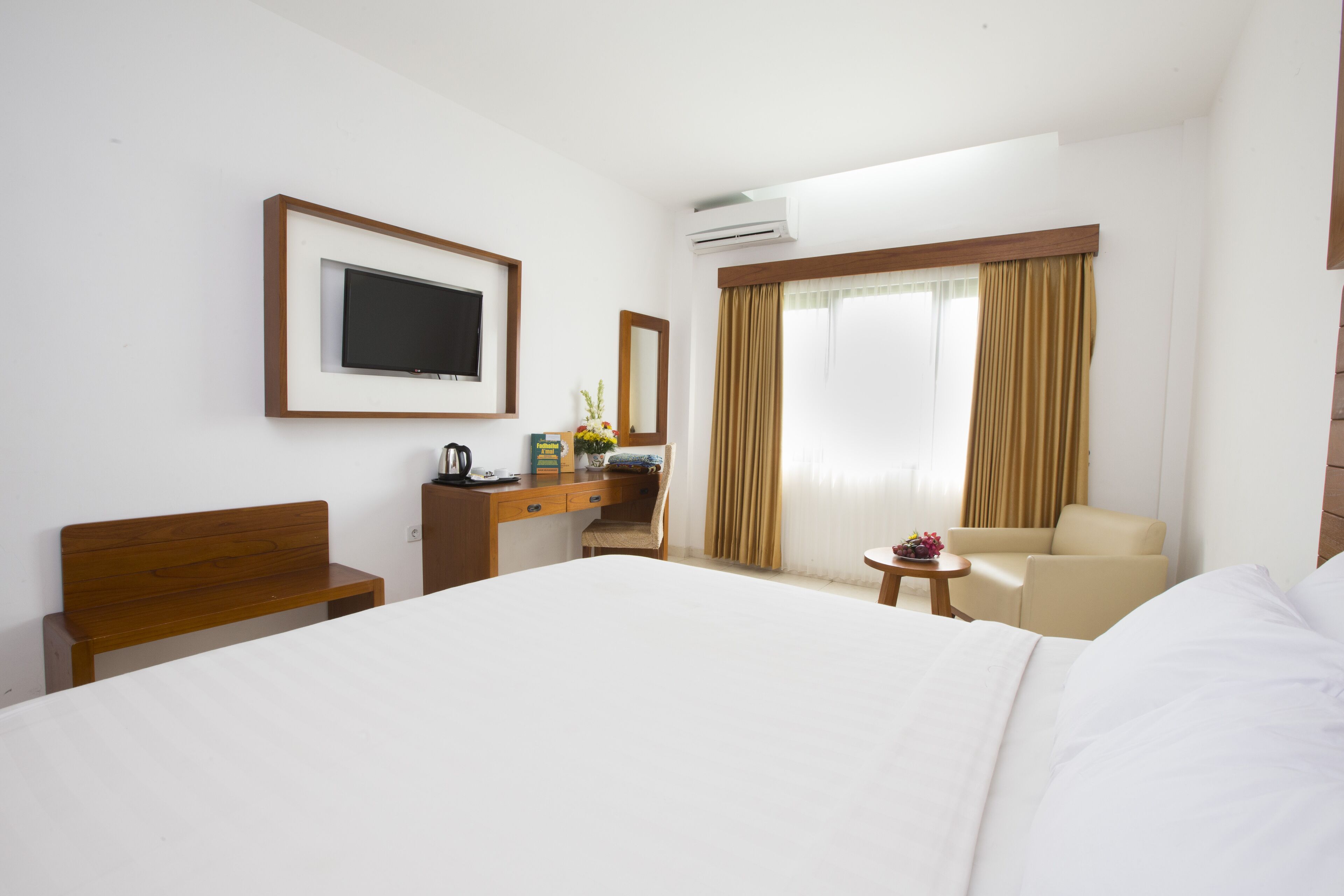 A hotel room with a large bed, a desk with a chair, a small table with a vase, and a sofa.