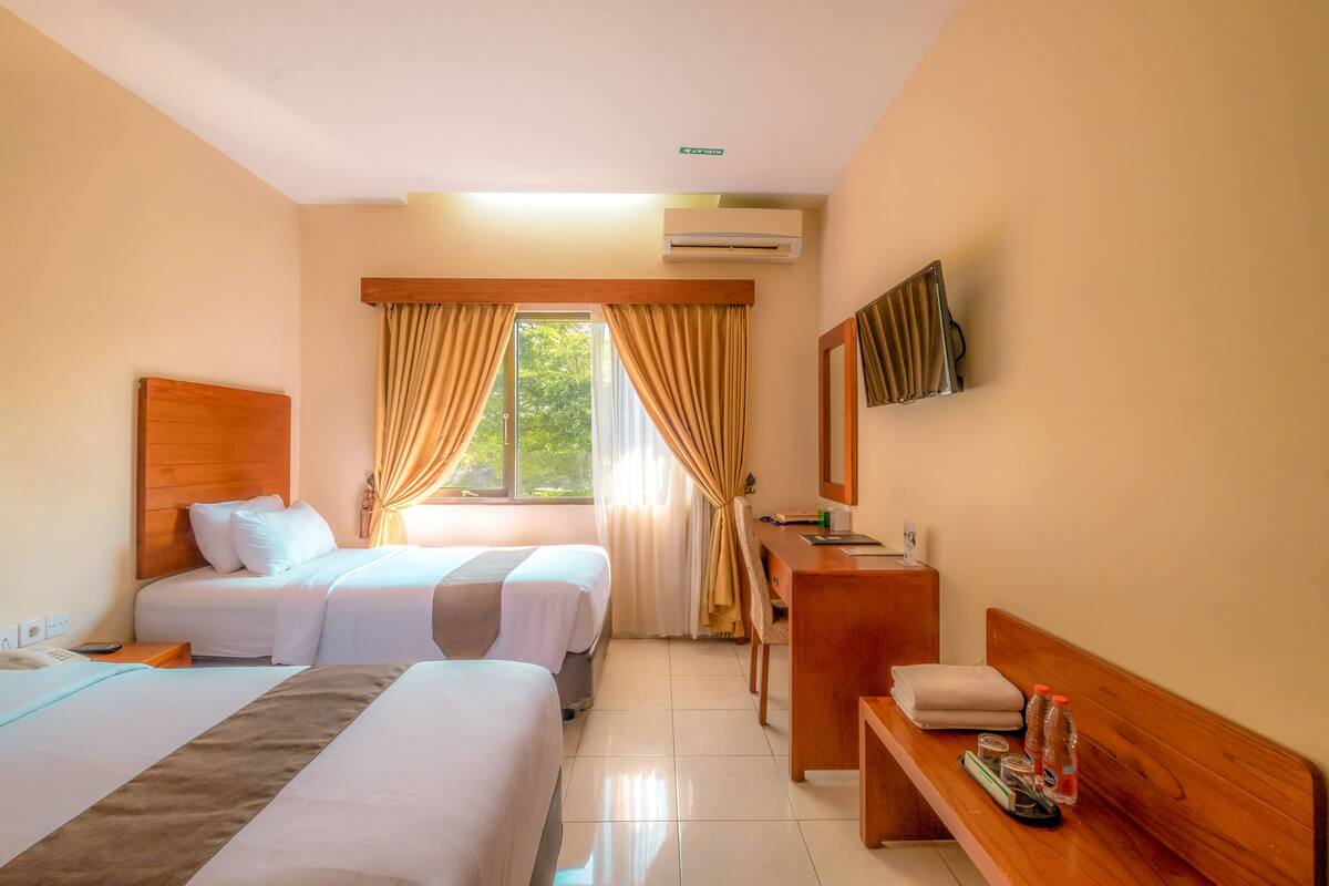 A hotel room with two beds, a desk, a chair, a mirror, and a window with curtains.