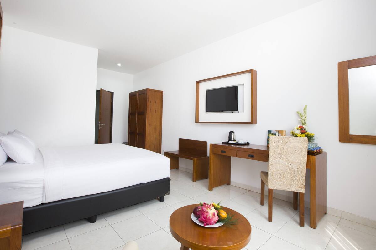 A hotel room with a bed, desk, chair, and a small table with fruit.