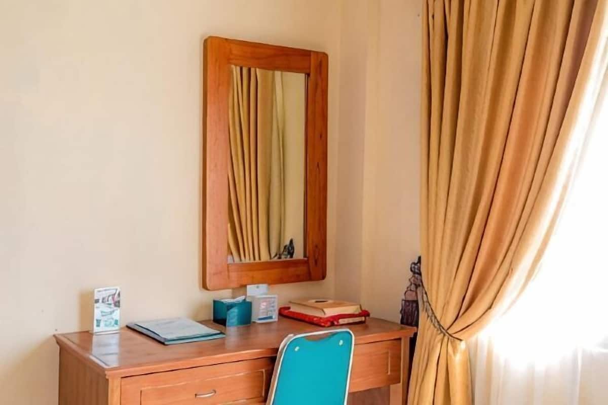 A wooden desk with a mirror, a blue chair, and a few items on the desk.