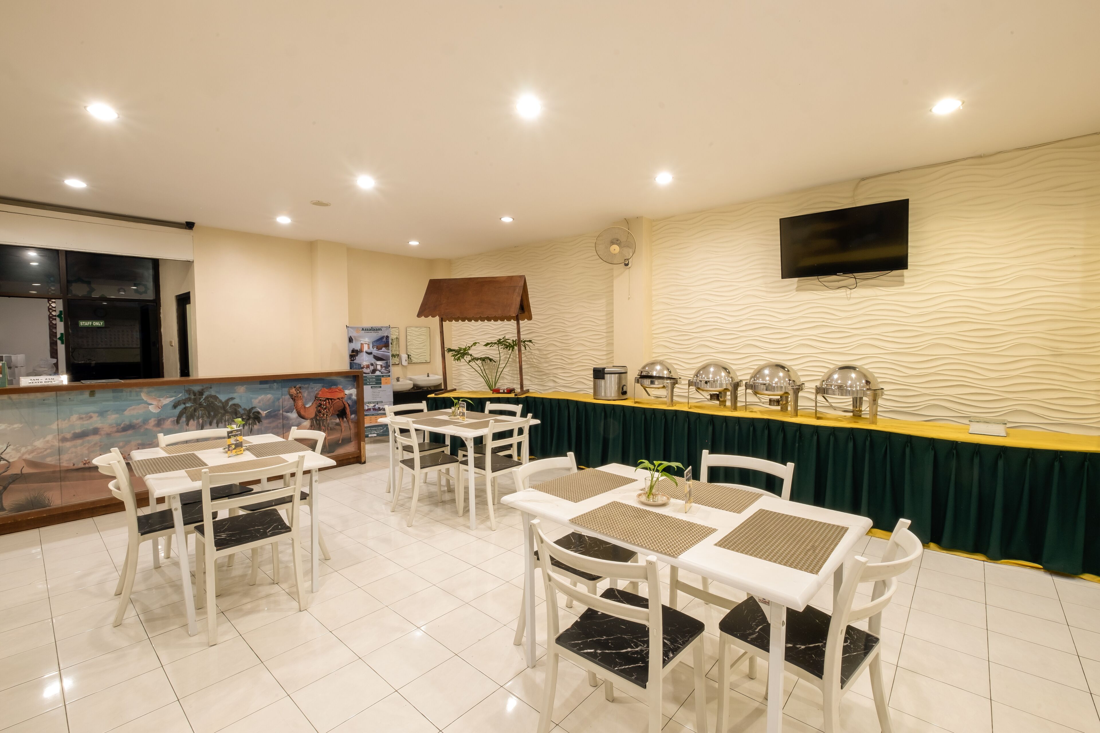 A dining area with white tables and chairs, a buffet counter, and a television mounted on the wall.