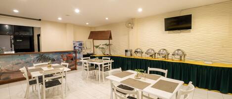 A dining area with white tables and chairs, a buffet counter, and a television mounted on the wall.