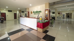 A reception area with a check-in counter, a red table with a plant, and a sign for Assalam Starrah Hotel. - Assalaam Syariah Hotel (Surakarta)