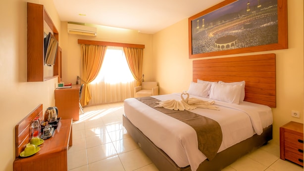 A hotel room with a bed, a desk with breakfast items, a painting of a cityscape, and a view of a building through the window. - Assalaam Syariah Hotel (Surakarta)
