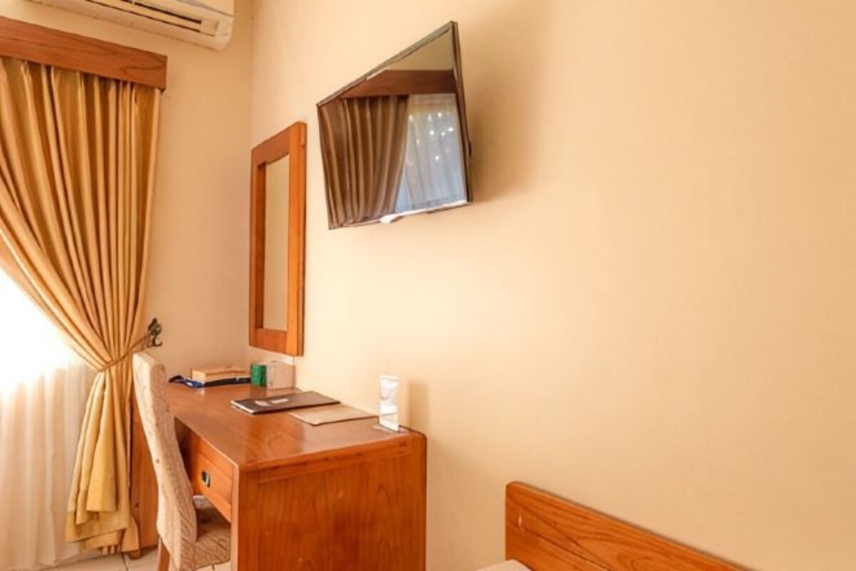 A hotel room with a wooden desk, a mirror, a bed, and a window with curtains.