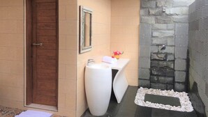 A bathroom with a wooden door, a white sink, a mirror, and a stone wall.
