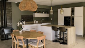 A modern kitchen with a central island, white cabinetry, and a dining area with a round wooden table and chairs.