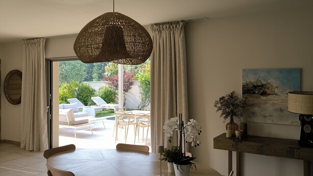 A dining area with a round table, chairs, a hanging light fixture, and a view of the outdoor patio.