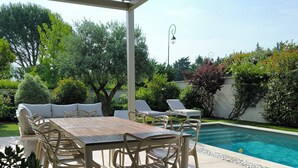 A covered patio with a pool table, chairs, and a pool.