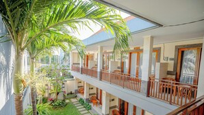 Un hôtel à plusieurs étages doté d’espaces extérieurs aménagés pour s’asseoir, d’un balcon couvert et d’un jardin bien entretenu.