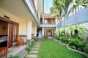 A two-story building with a balcony, a staircase, and a small garden area with plants and a pathway. - Sakura Guesthouse (Tibubeneng)
