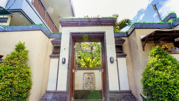 Une entrée d’immeuble agrémentée d’une arche décorative, d’un escalier menant à l’entrée et d’un petit jardin avec une statue.