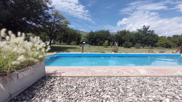 Ein Swimmingpool mit glatter, blauer Wasserfläche, umgeben von Kiesflächen und einer Rasenfläche.