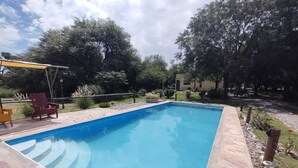 Ein rechteckiger Pool mit Steinrand, umgeben von einer Terrasse mit Stühlen und einer Pergola.