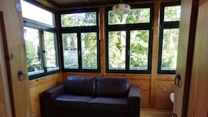 Een houten kamer met een donker leren bank, een kamerbreed tapijt met dessin en grote ramen met uitzicht op groen.