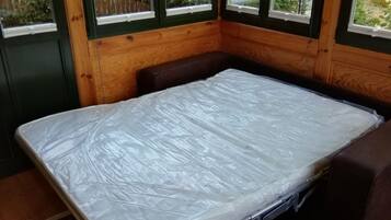 Una habitación pequeña con una cama, un banco y ventanas grandes.