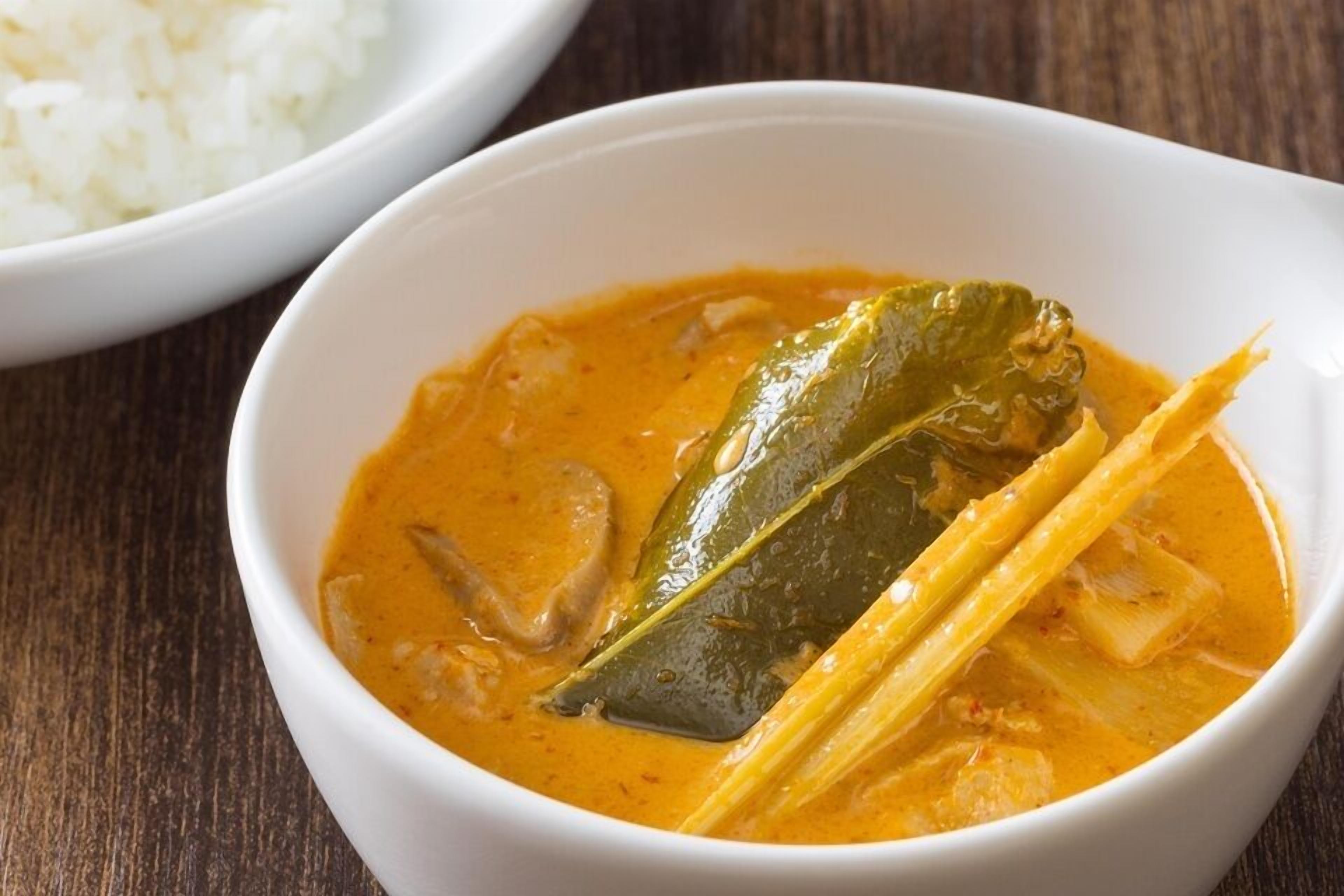 A bowl of curry with a bay leaf and a piece of lemongrass, served with white rice.