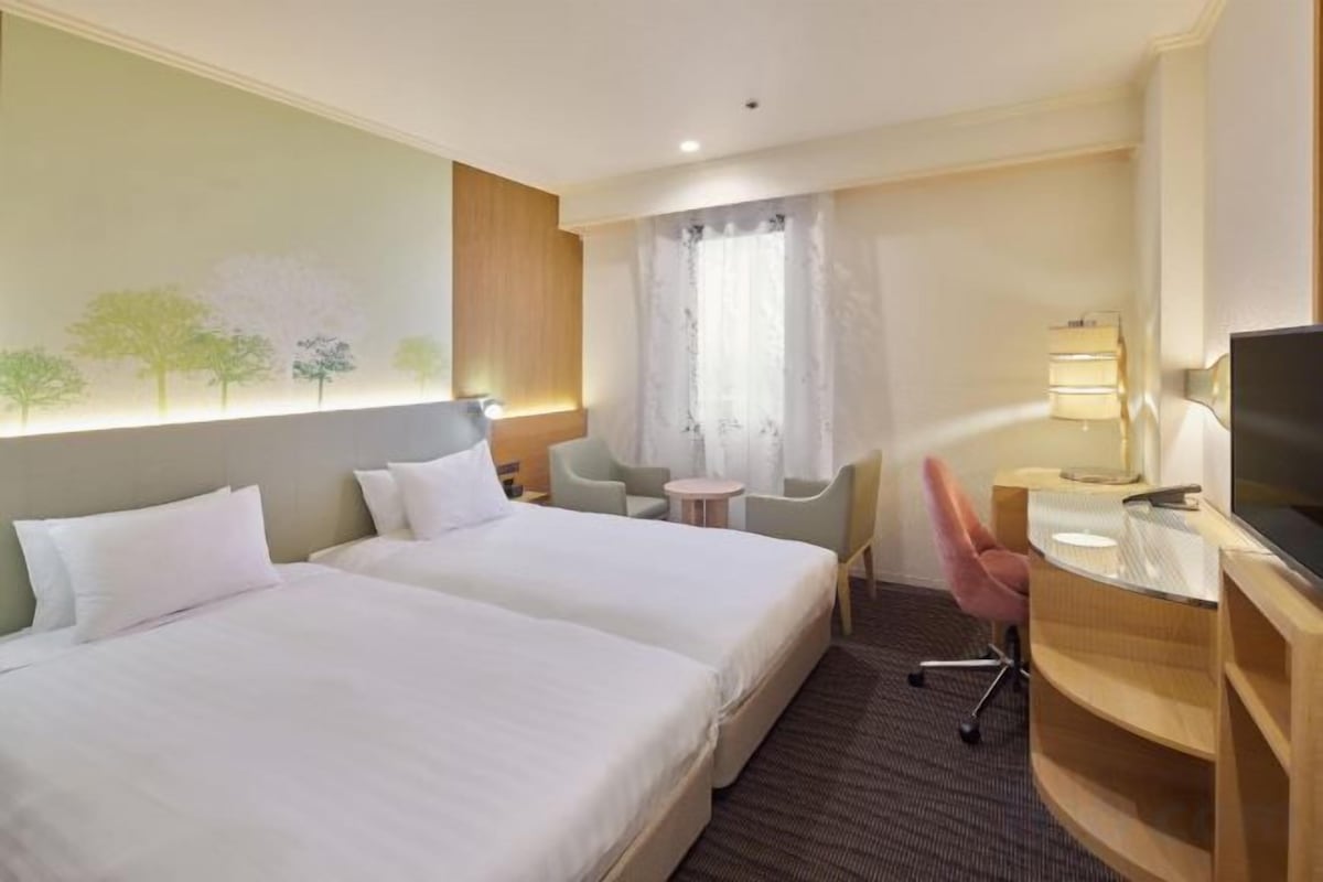 Een hotelkamer met twee bedden, een bureau met stoel, een televisie en een klein tafeltje.
