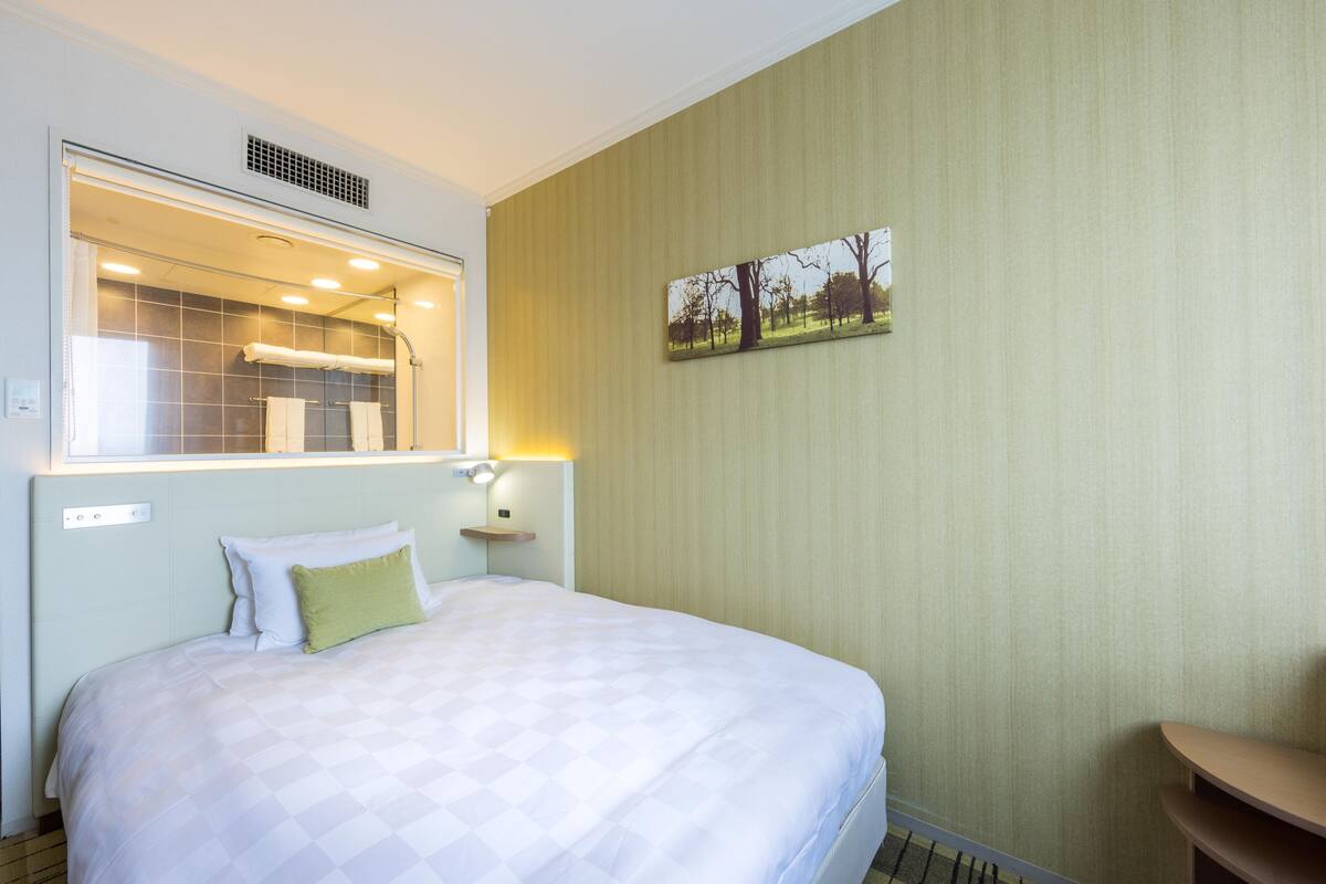 A hotel room with a large bed, a bathroom with a shower, and a painting on the wall.