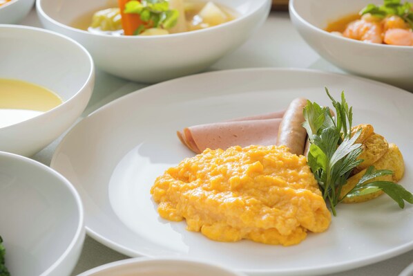 A breakfast setting with scrambled eggs, ham, and a side of vegetables on a plate.
