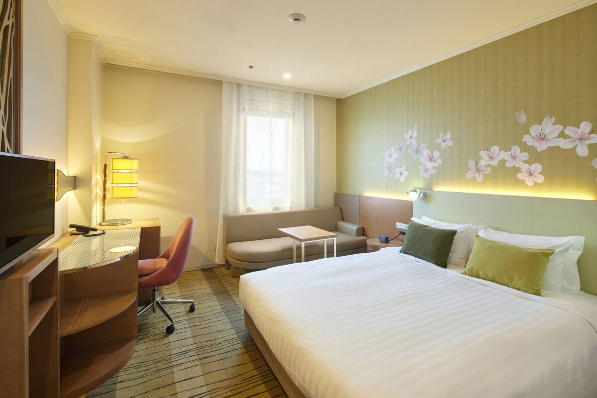 A hotel room with a bed, a desk, a chair, a TV, and a window with curtains.