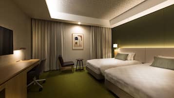 A hotel room with two beds, a desk, a chair, a small table, and a wall-mounted TV.