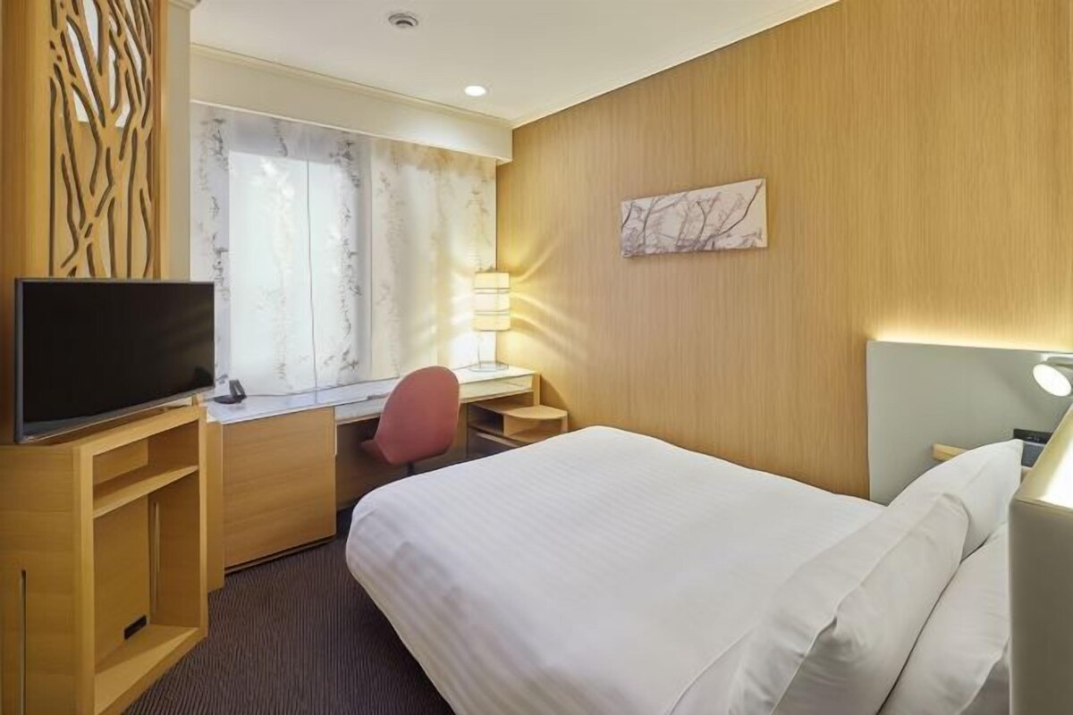 Een hotelkamer met een bed, een bureau met een computer, een televisie en een lamp.