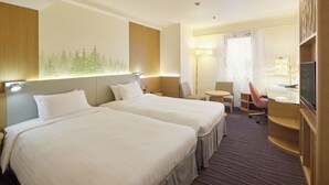 Habitación de hotel con dos camas, un escritorio, una silla, un televisor y un ventanal con un mural de un bosque.