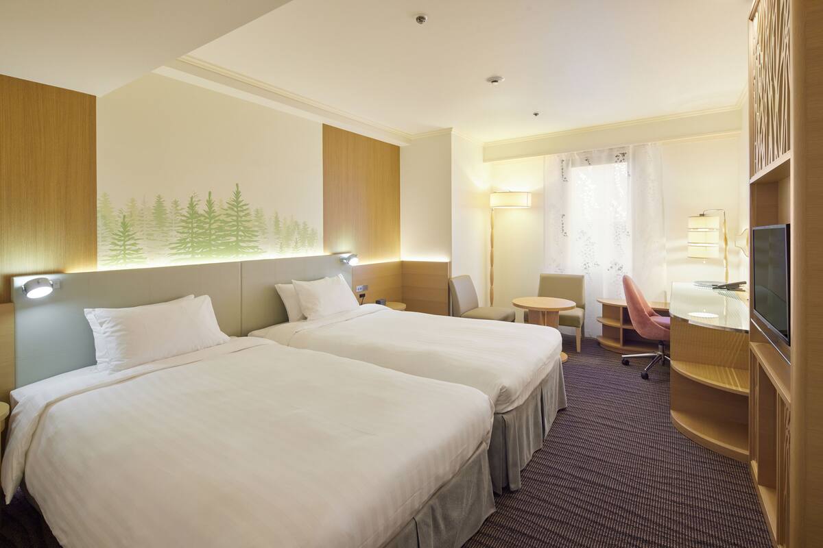 A hotel room with two beds, a desk, a chair, a TV, and a window with a forest mural.