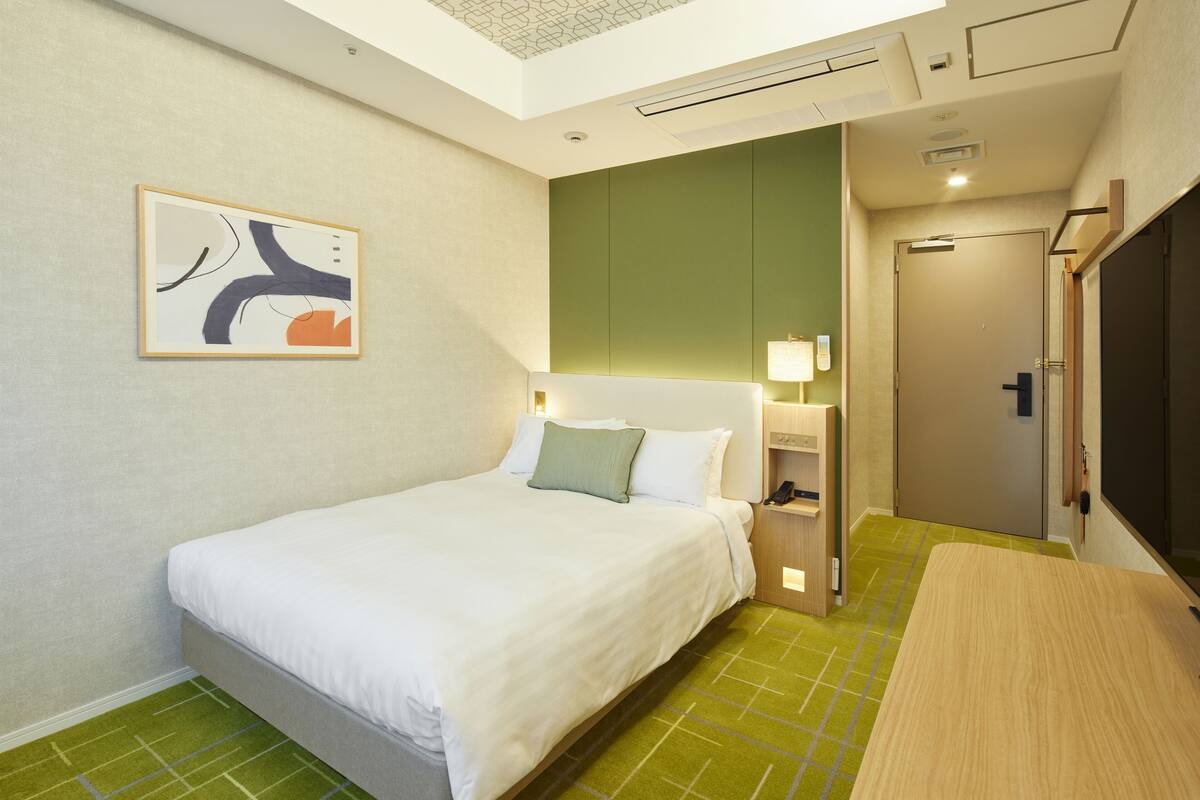 A hotel room with a bed, a bedside table, a lamp, and a green floor.