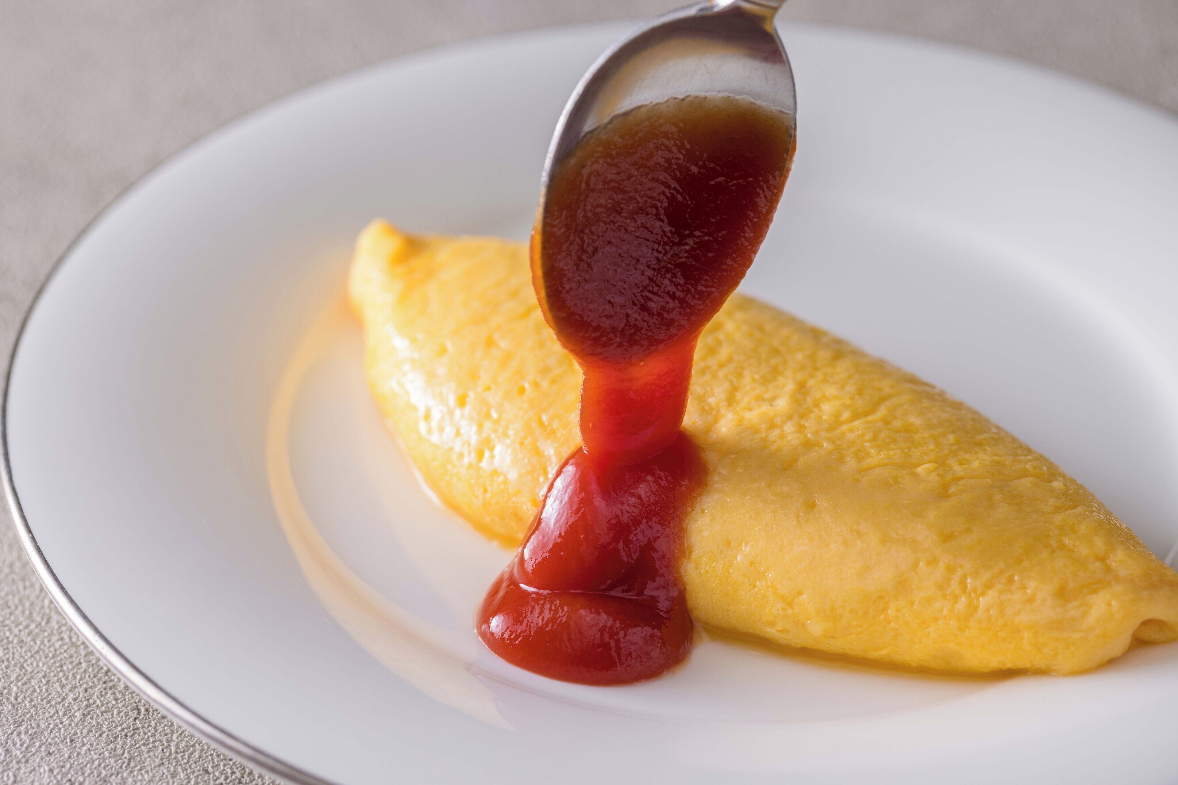 A plate with a folded omelette and a spoonful of ketchup.