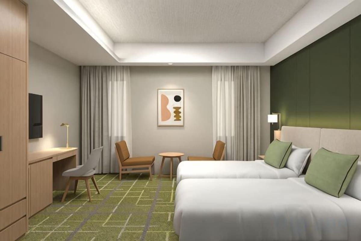 A hotel room with two beds, a desk, a chair, a small table, and a TV.